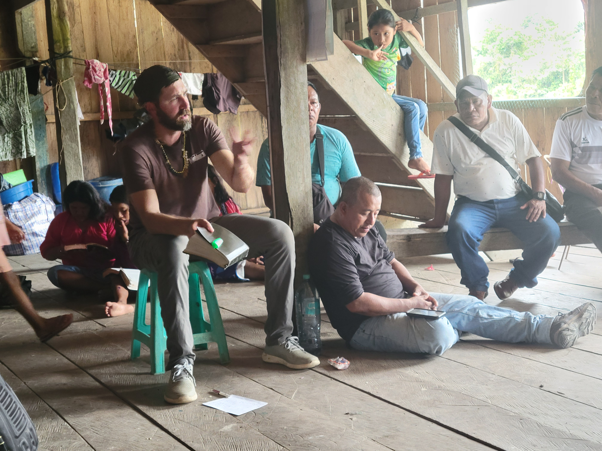 Man teaching from Scripture inside a wooden village home while families listen