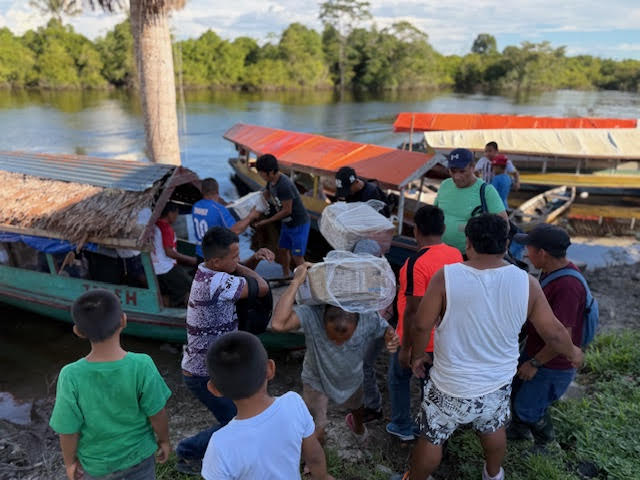 Men helping unload a suitcase from a small boat onto a log dock