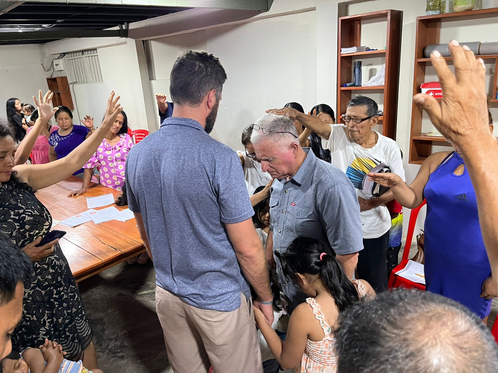 Group laying hands and praying for an older man in a church meeting room
