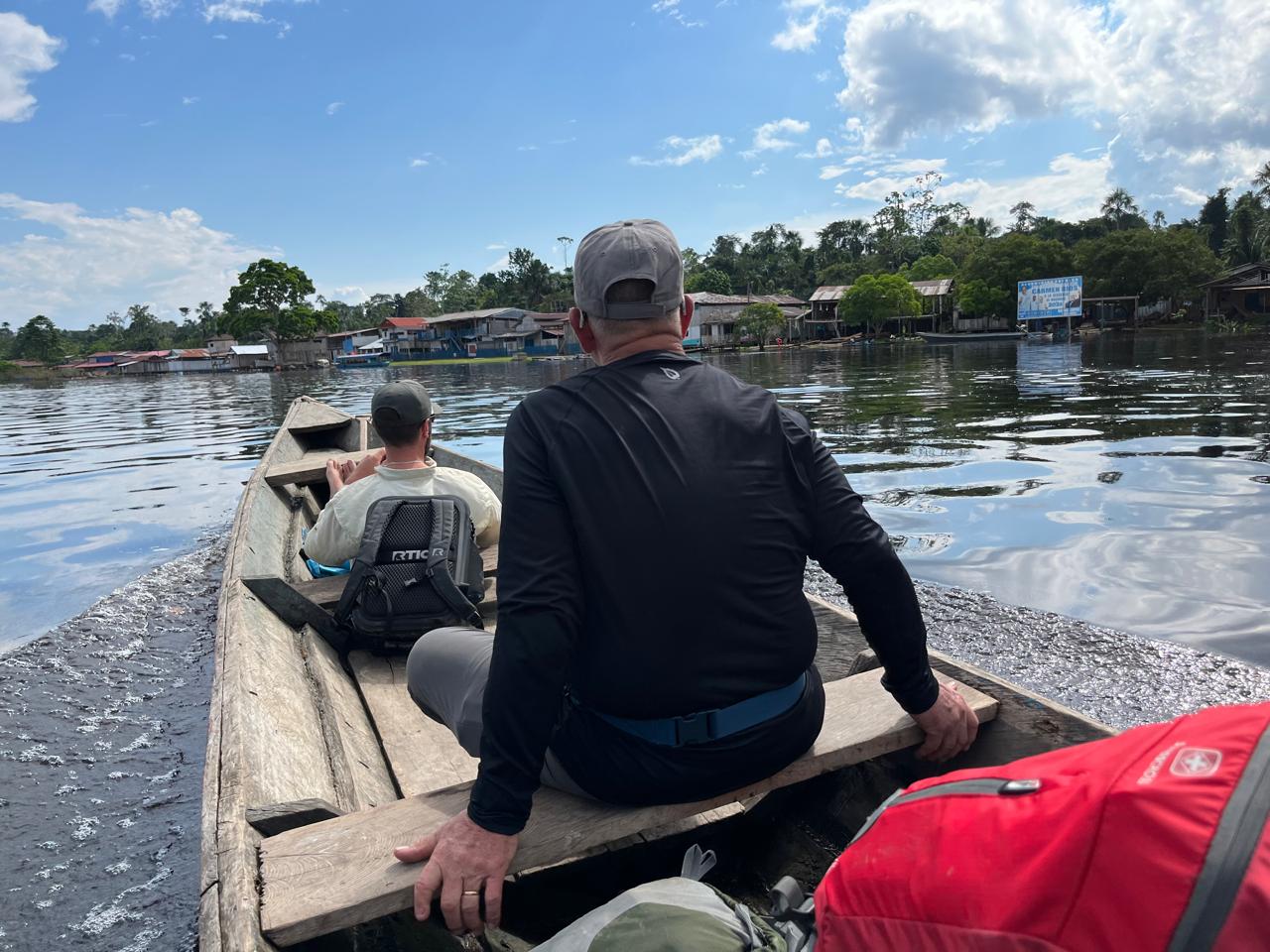 Two men in rain jackets waving from a small motor boat with a local guide
