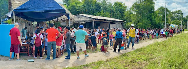 Wide view of a village street lined with families waiting for the clinic