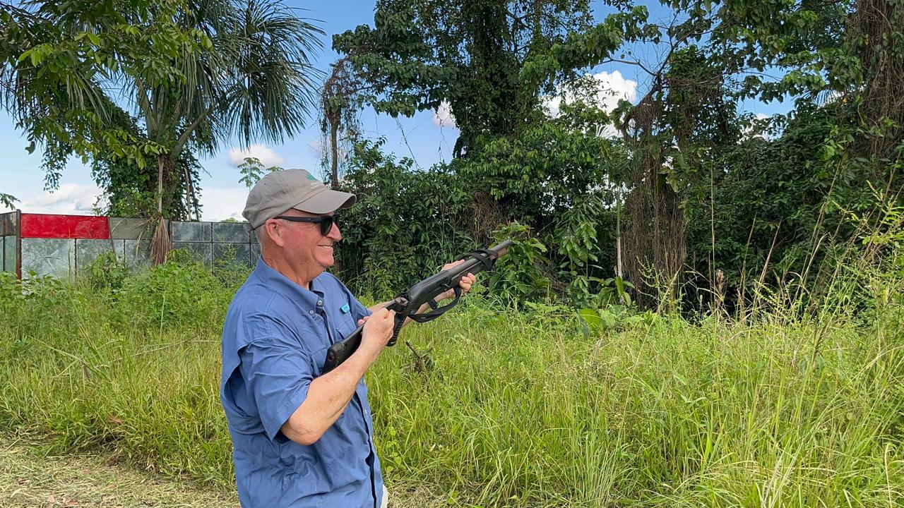 David smiling and holding a shotgun on a sunny day in a grassy clearing